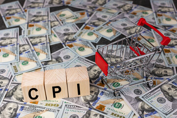 Wooden block with the word cpi and an empty shopping cart on a banknotes of dollar background....
