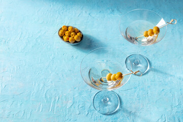 Martini, two glasses with spicy olives, on a blue background. Alcoholic cold drink with copy space