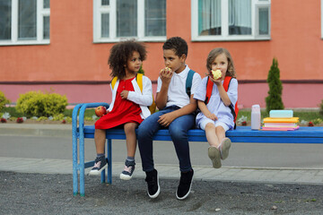 Fototapeta premium Cute Black schoolboy and girls are eating outdoors next the school.
