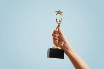 woman hand raised, holding gold star cup against sky. award and victory concept