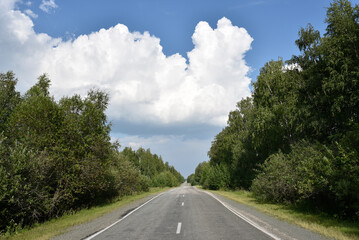 Fototapeta premium Thunderclouds on a summer day and a road in the countryside. A thunderstorm on a bright day.