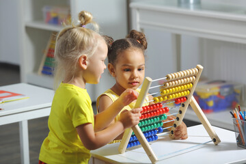 children of different races sit together at the table and count on the abacus - obrazy, fototapety, plakaty