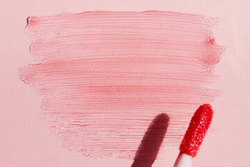 Smears of shining lip gloss and lip gloss brush on pink background, hard shadows