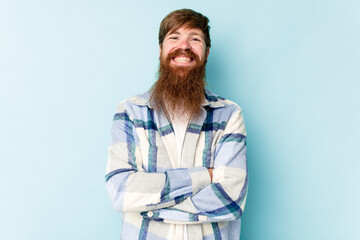Young caucasian red-haired man isolated on blue background who feels confident, crossing arms with determination.