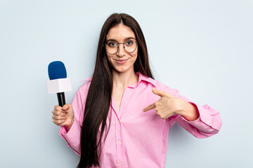 Fototapeta na wymiar Young caucasian tv presenter woman isolated on blue background person pointing by hand to a shirt copy space, proud and confident