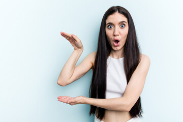 Young caucasian woman isolated on blue background shocked and amazed holding a copy space between hands.