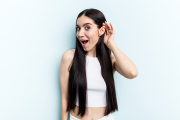 Fototapeta premium Young caucasian woman isolated on blue background trying to listening a gossip.