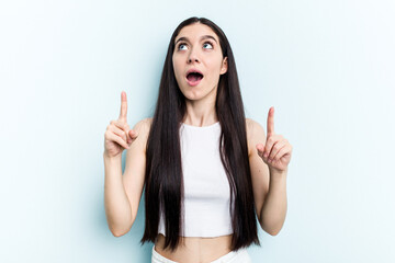 Young caucasian woman isolated on blue background pointing upside with opened mouth.