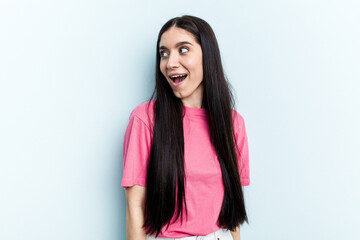 Young caucasian woman isolated on blue background looks aside smiling, cheerful and pleasant.