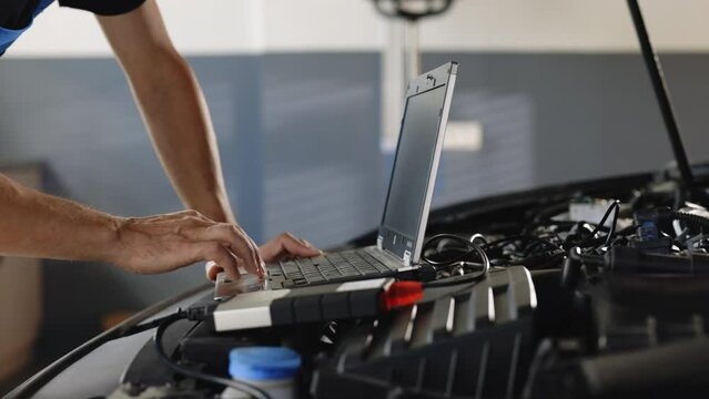 Computer diagnostics of the car. European car mechanic holds a digital device. Auto mechanic uses laptop while conducting diagnostics test. Modern car service