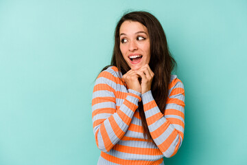 Young caucasian woman isolated on blue background praying for luck, amazed and opening mouth looking to front.