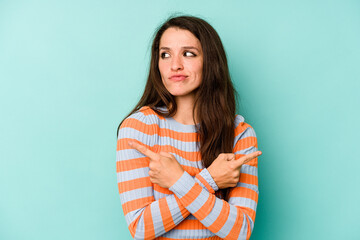 Young caucasian woman isolated on blue background points sideways, is trying to choose between two options.