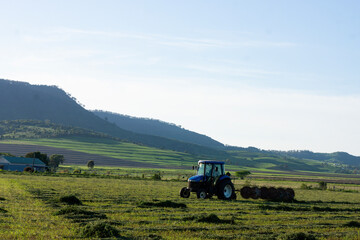 Man on his tractor raking hay against a backdrop of lush countryside in Southern Queensland on a...