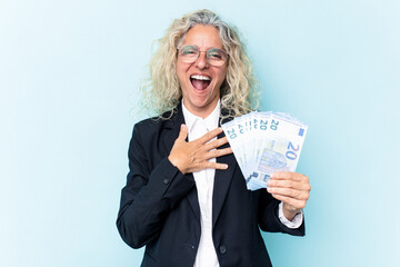 Middle age business caucasian woman holding bank notes isolated on white background laughs out loudly keeping hand on chest.