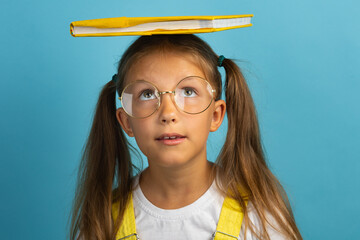 Caucasian girl in glasses schoolgirl with a book on her head