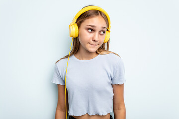 Young caucasian girl listening to music isolated on blue background confused, feels doubtful and unsure.