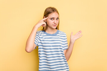 Young caucasian girl isolated on yellow background holding and showing a product on hand.