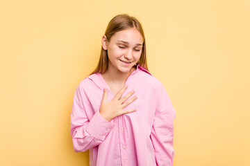 Young caucasian girl isolated on yellow background laughs out loudly keeping hand on chest.