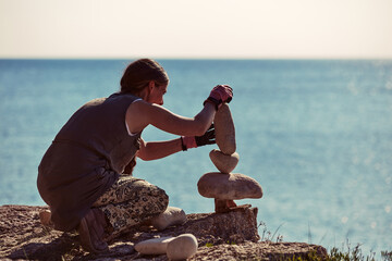 Woman balancing stones on the ocean sea coast.