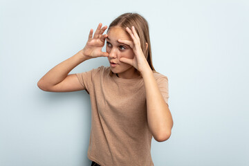 Young caucasian girl isolated on blue background keeping eyes opened to find a success opportunity.