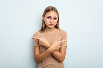 Obraz premium Young caucasian girl isolated on blue background points sideways, is trying to choose between two options.