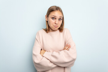 Young caucasian girl isolated on blue background shrugs shoulders and open eyes confused.