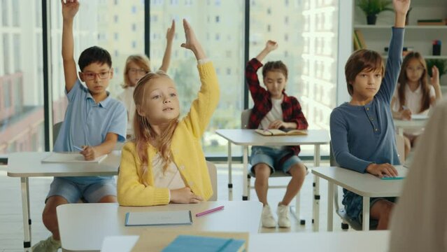 Junior school students raise their hand in class to answer the teacher's question. Children know the answer to the question and raise their hand to answer it. People and educational concept.