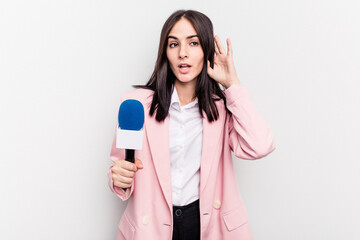 Young TV presenter caucasian woman isolated on white background trying to listening a gossip.