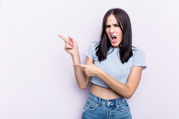 Young caucasian woman isolated on pink background pointing with forefingers to a copy space, expressing excitement and desire.