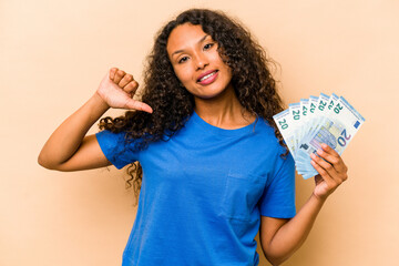 Young hispanic woman holding bank notes isolated on beige background feels proud and self confident, example to follow.