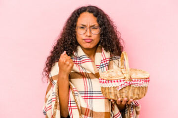 Young hispanic woman doing a picnic isolated on beige background showing fist to camera, aggressive facial expression.