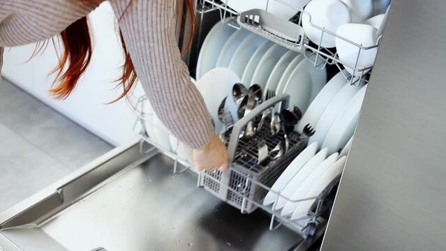 A young woman closes the dishwasher with white dishes. Build into the kitchen. Modern home kitchen. Housework. Slow motion
