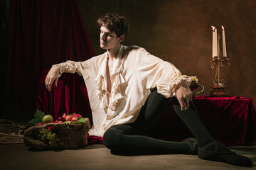 Artistic portrait of young handsome man in image of famous historical character, medieval person isolated on dark vintage background. Retro style