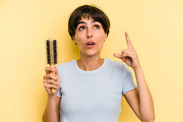 Young caucasian woman holding a brush hair isolated on yellow background pointing upside with opened mouth.