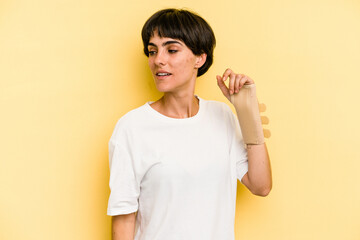 Young caucasian woman hand sling isolated on yellow background looks aside smiling, cheerful and pleasant.