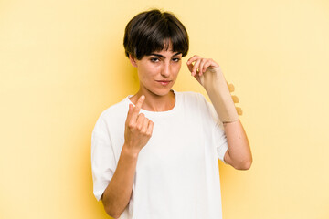 Young caucasian woman hand sling isolated on yellow background pointing with finger at you as if...
