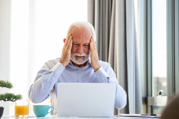 Stressed mature businessman with laptop. He could also have a headache. He is sitting in the...