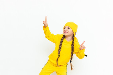 A little girl in a hat and a yellow suit points to your advertisement on a white isolated background. Autumn clothes for children. Copy space.