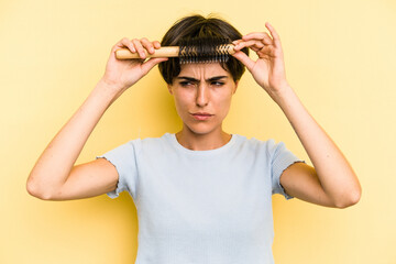 Young caucasian woman holding a brush hair isolated on yellow background
