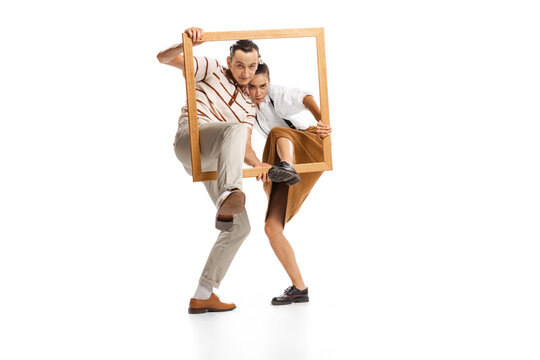 Portrait of man and woman appearing from picture frame, posing isolated over white background. Retro style