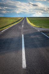  The concrete road leading through the countryside environment with natural scenery of forest and agricultural fields. Country road experience.