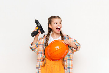 A little girl with an electric screwdriver in a protective orange construction helmet smiles broadly on a white isolated background. The concept of renovation in the room of a teenage girl.