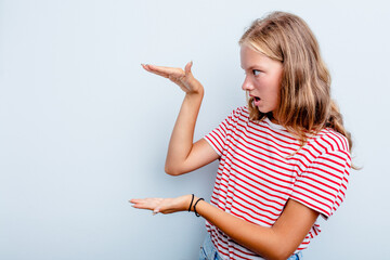 Caucasian teen girl isolated on blue background shocked and amazed holding a copy space between hands.