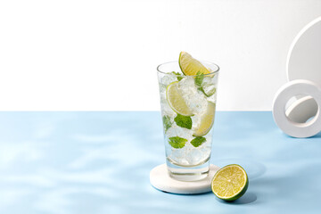Mojito, Iced cold summer drink on podium. Glass of cold tonic with lime. Lemonade with ice and mint on blue background. Copy space