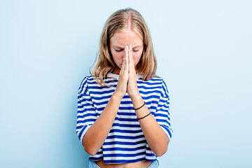 Caucasian teen girl isolated on blue background praying, showing devotion, religious person looking for divine inspiration.