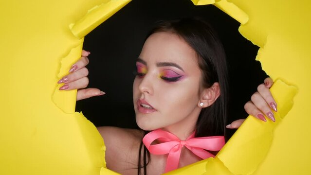 A beautiful young girl model with a bright juicy yellow fashion make-up and a pink bow around her neck on a background of stylish yellow paper. Fashion model image