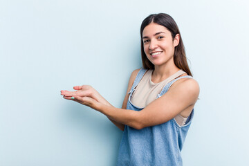 Young caucasian woman isolated on blue background holding a copy space on a palm.