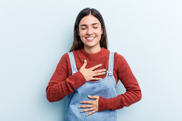 Young caucasian woman isolated on blue background laughs happily and has fun keeping hands on...