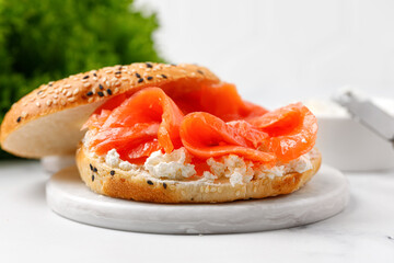 Bagel sandwich with salmon and cream cheese on marble board and white background