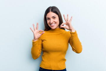 Young caucasian woman isolated on blue background cheerful and confident showing ok gesture.